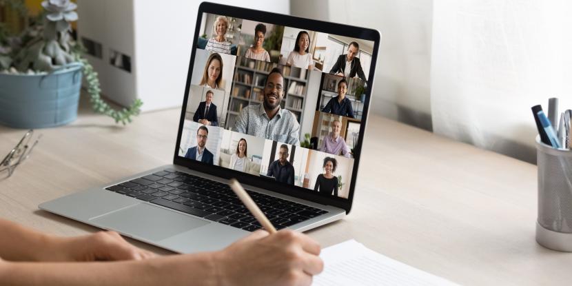 Virtual meeting displayed on a laptop with a person's arm visible taking notes