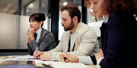 Three people sitting at a table taking notes during a meeting